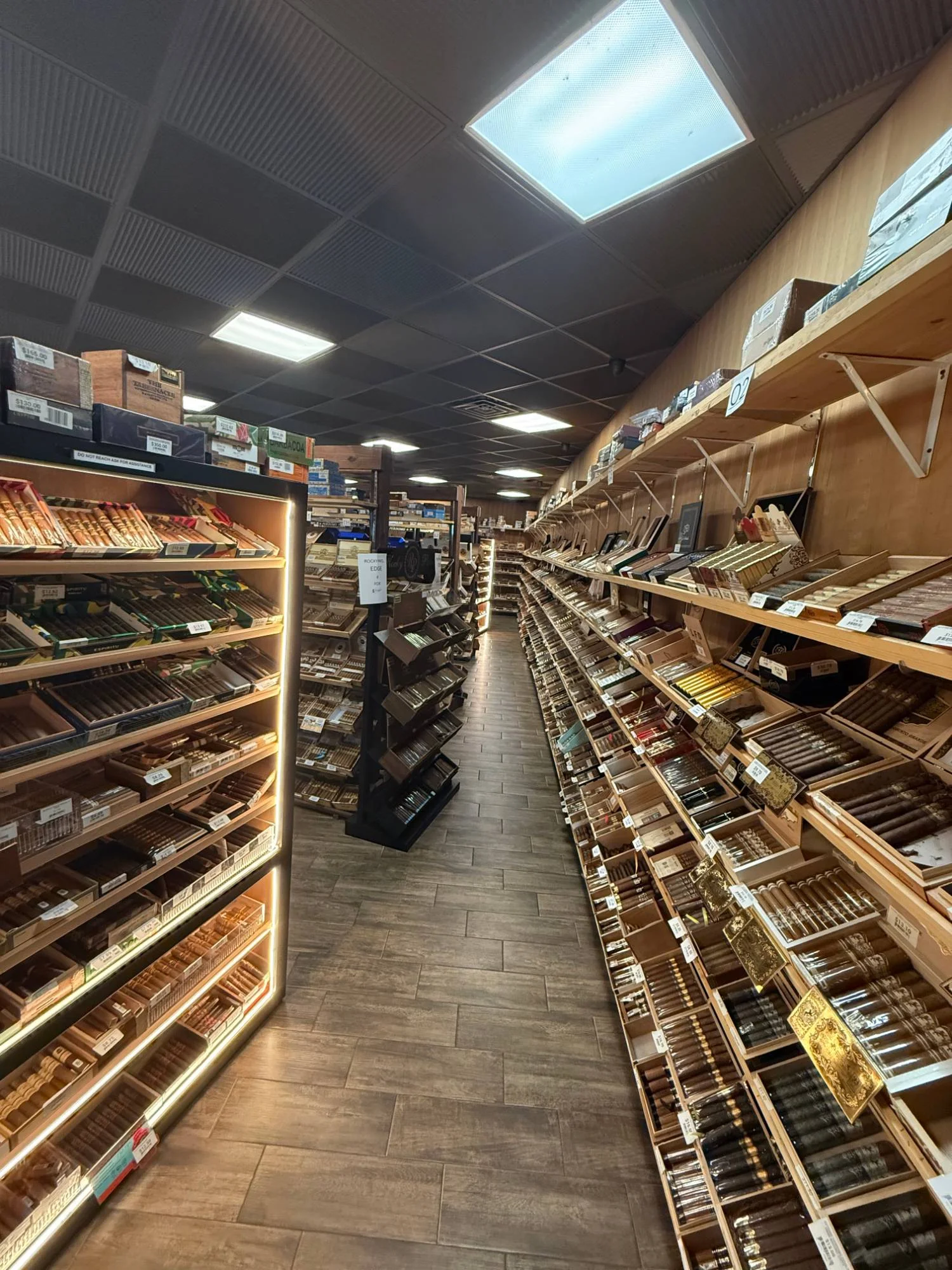 A long aisle in the Cigar Heaven humidor — a lit display case on the left and a full wall of open cigar boxes on the right.