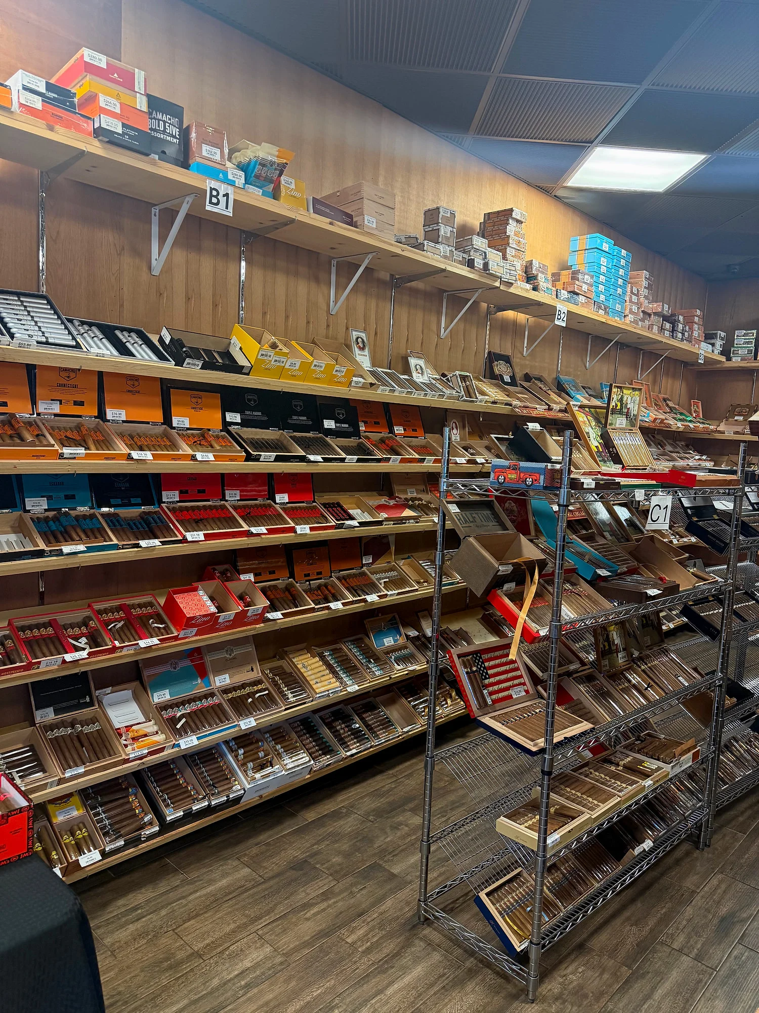 Wall shelves stacked with Camacho and other boxes, with a wire rack of boutique cigars in front, at Cigar Heaven.