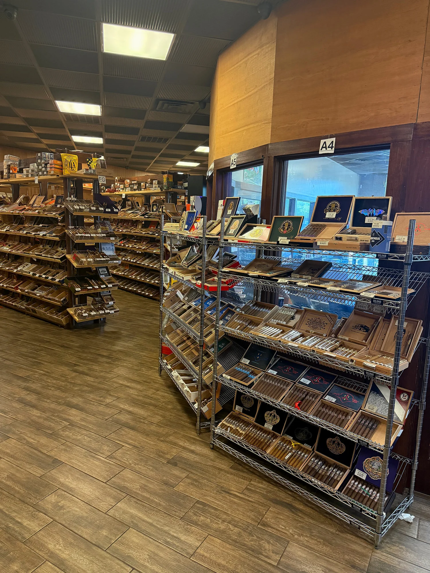 Wire racks of boutique brands along the humidor windows at Cigar Heaven, with wooden shelving islands behind.