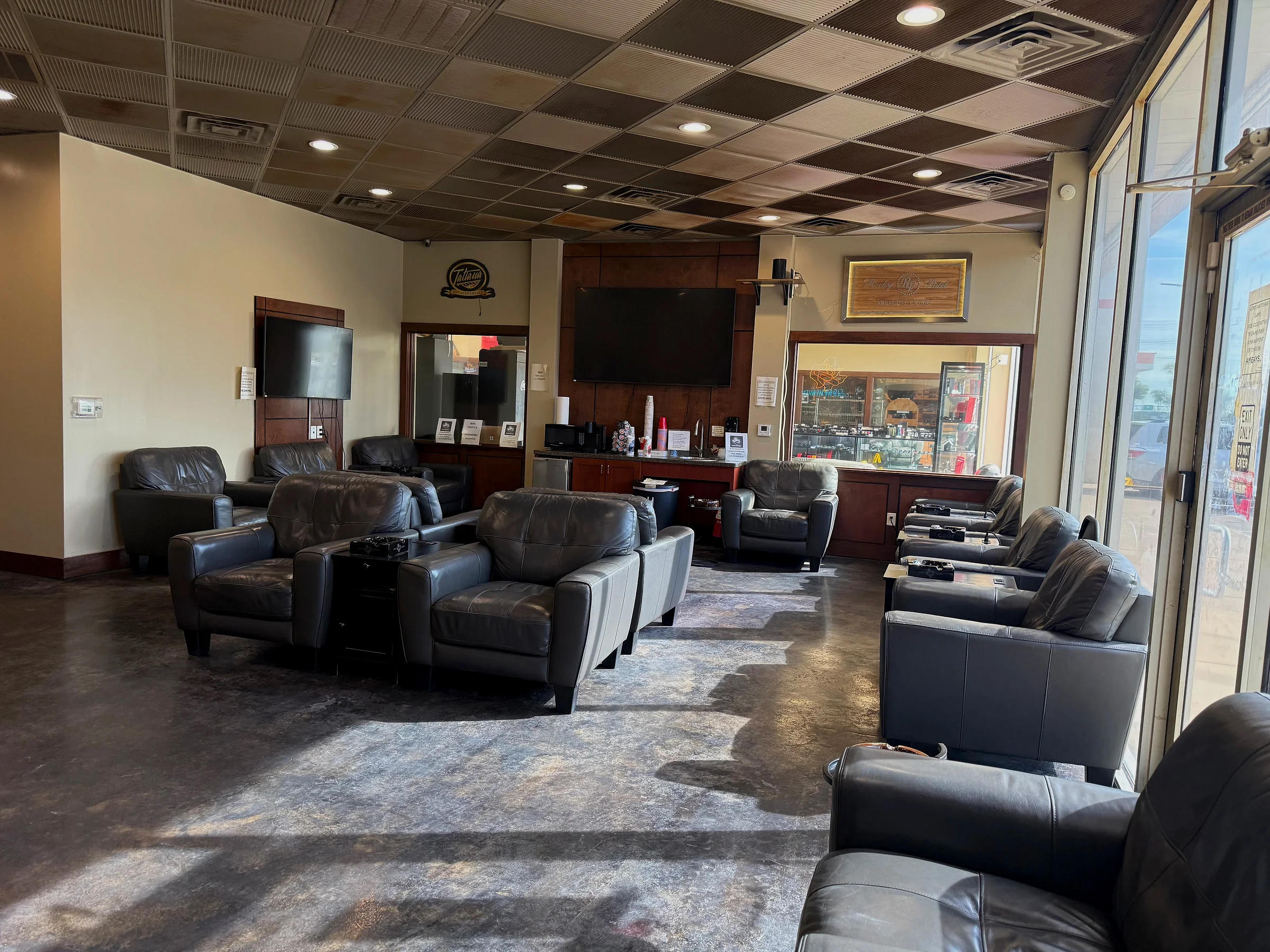 Leather armchairs along the front windows of the Cigar Heaven lounge, with the coffee station and a large TV on the back wall.