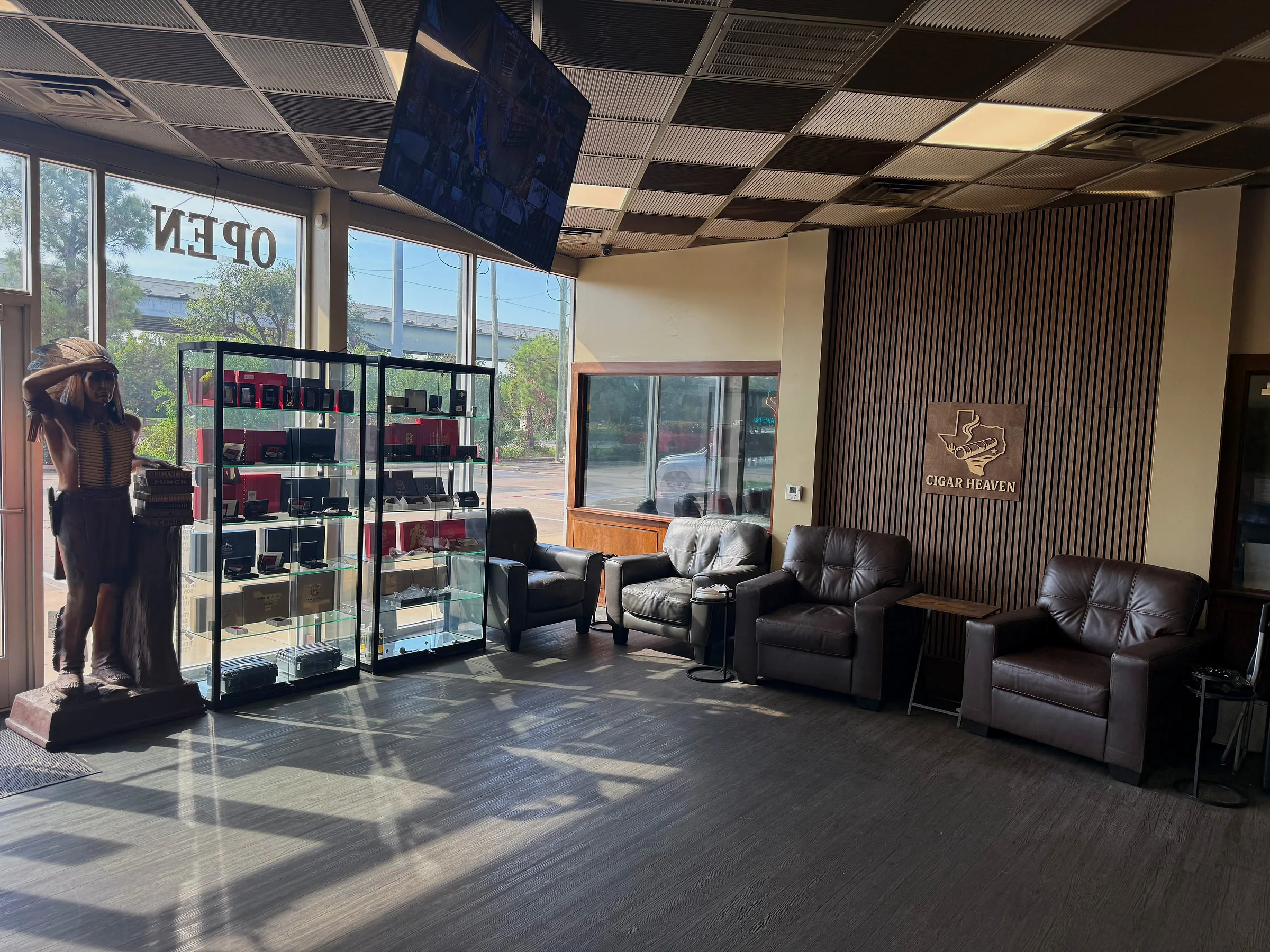 The front of Cigar Heaven — glass display cases, brown leather armchairs and the wooden Cigar Heaven sign on a slatted wall.