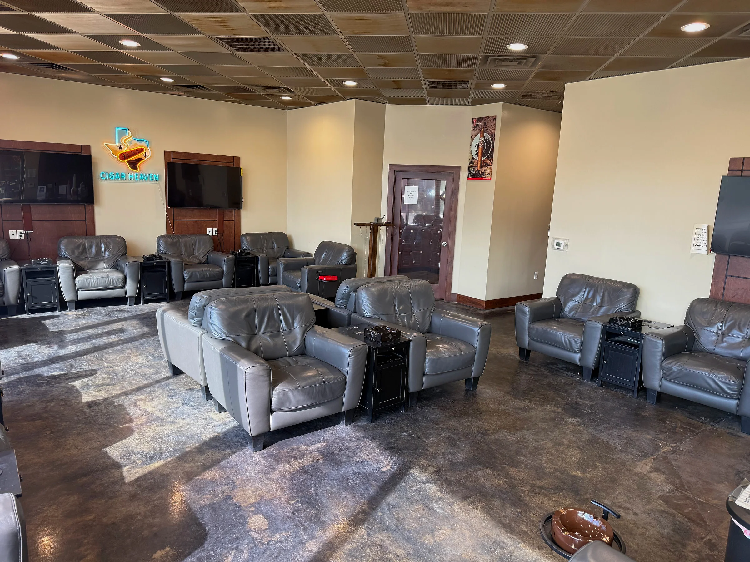 Wide view of the Cigar Heaven lounge — clusters of leather armchairs with side tables and ashtrays under recessed lights.