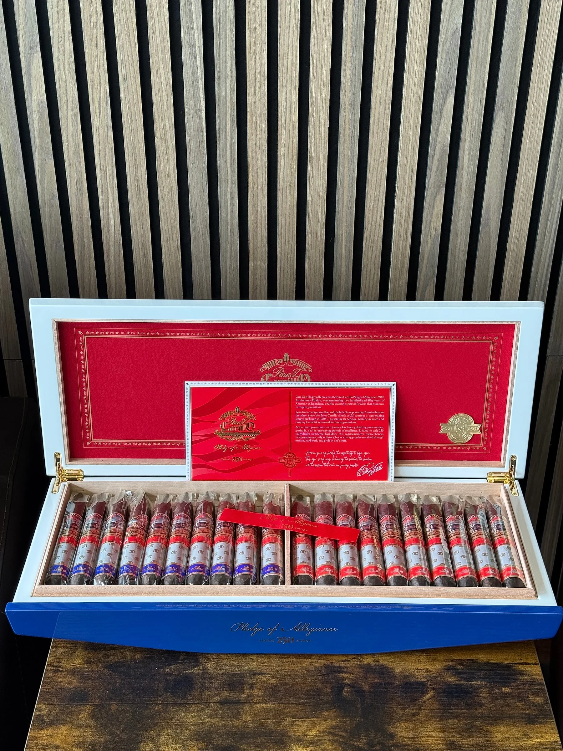 An open white-and-blue humidor of Casa Carrillo Pledge of Allegiance 250th Anniversary cigars, with a red certificate card, in the Cigar Heaven lounge.