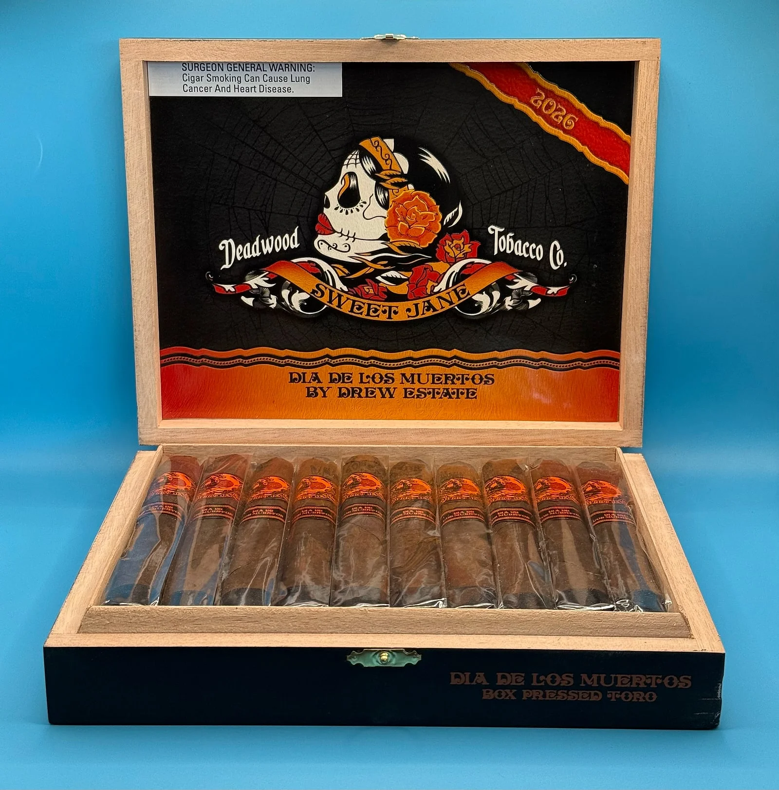 An open box of Deadwood Sweet Jane Día de los Muertos 2026 box-pressed toros by Drew Estate, with a sugar-skull lady on the lid.