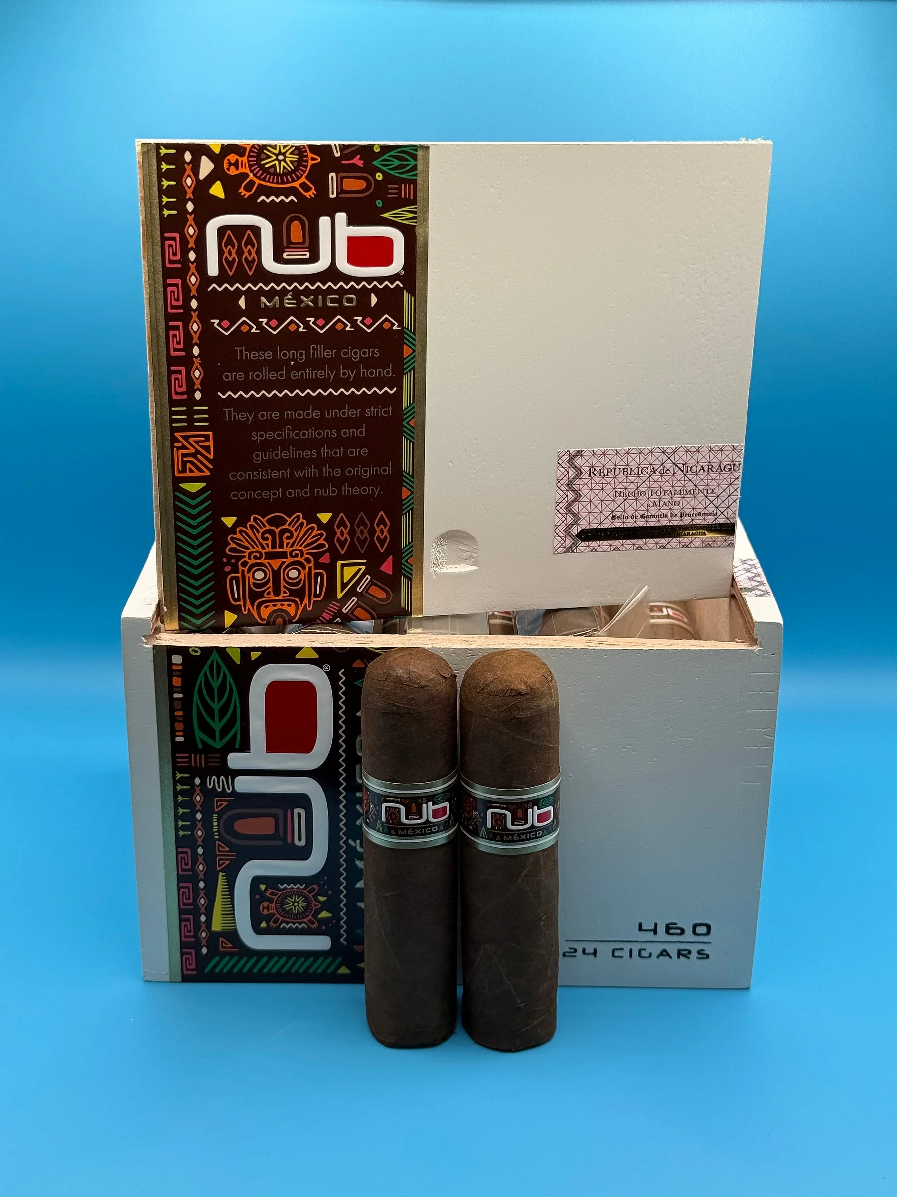 Two Nub México 460 cigars in front of an open white box of 24, decorated with colorful Mexican patterns.