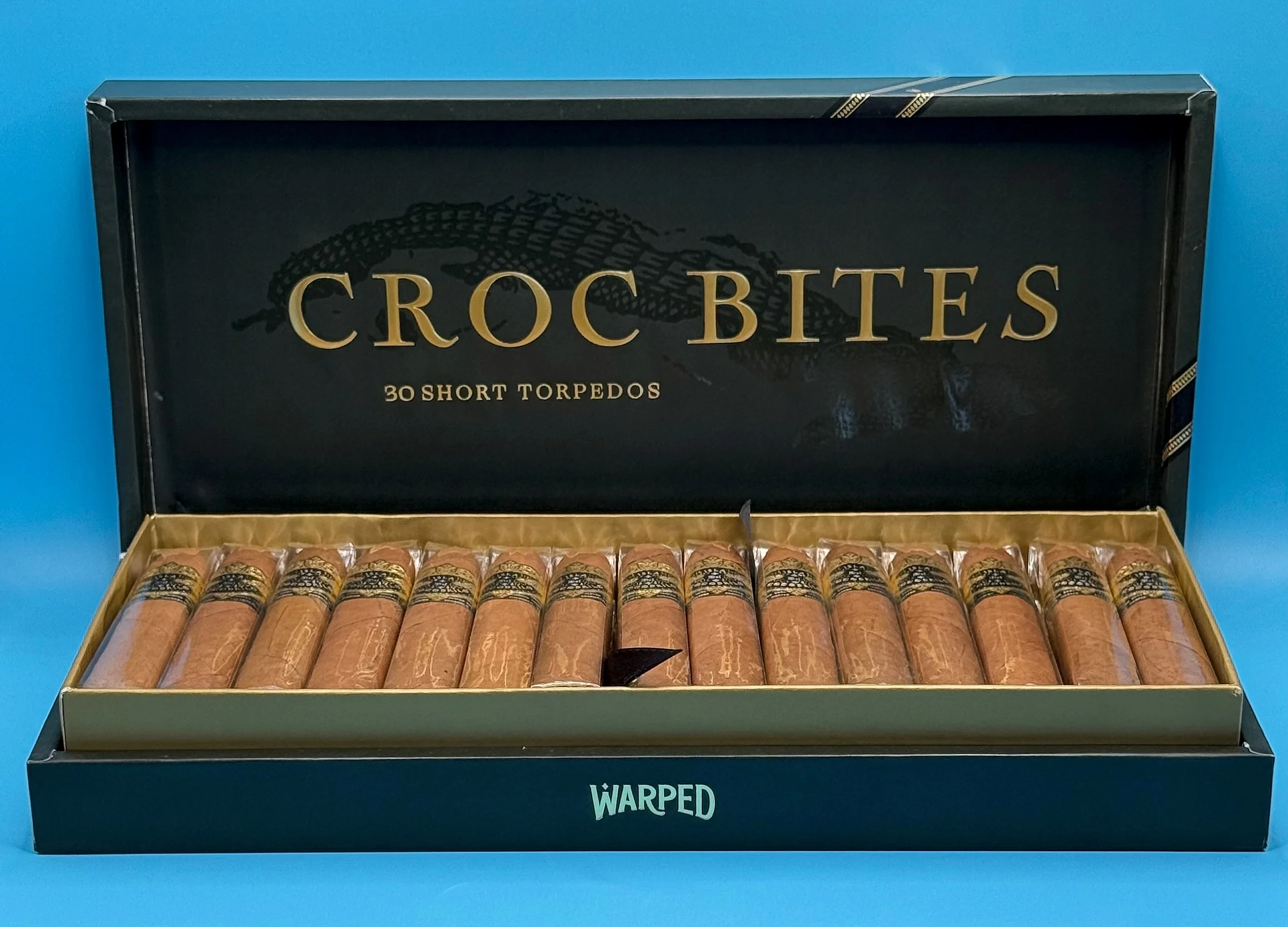 An open box of Warped Isla del Cocodrilo Croc Bites short torpedos, 30 count, with a crocodile printed inside the lid.